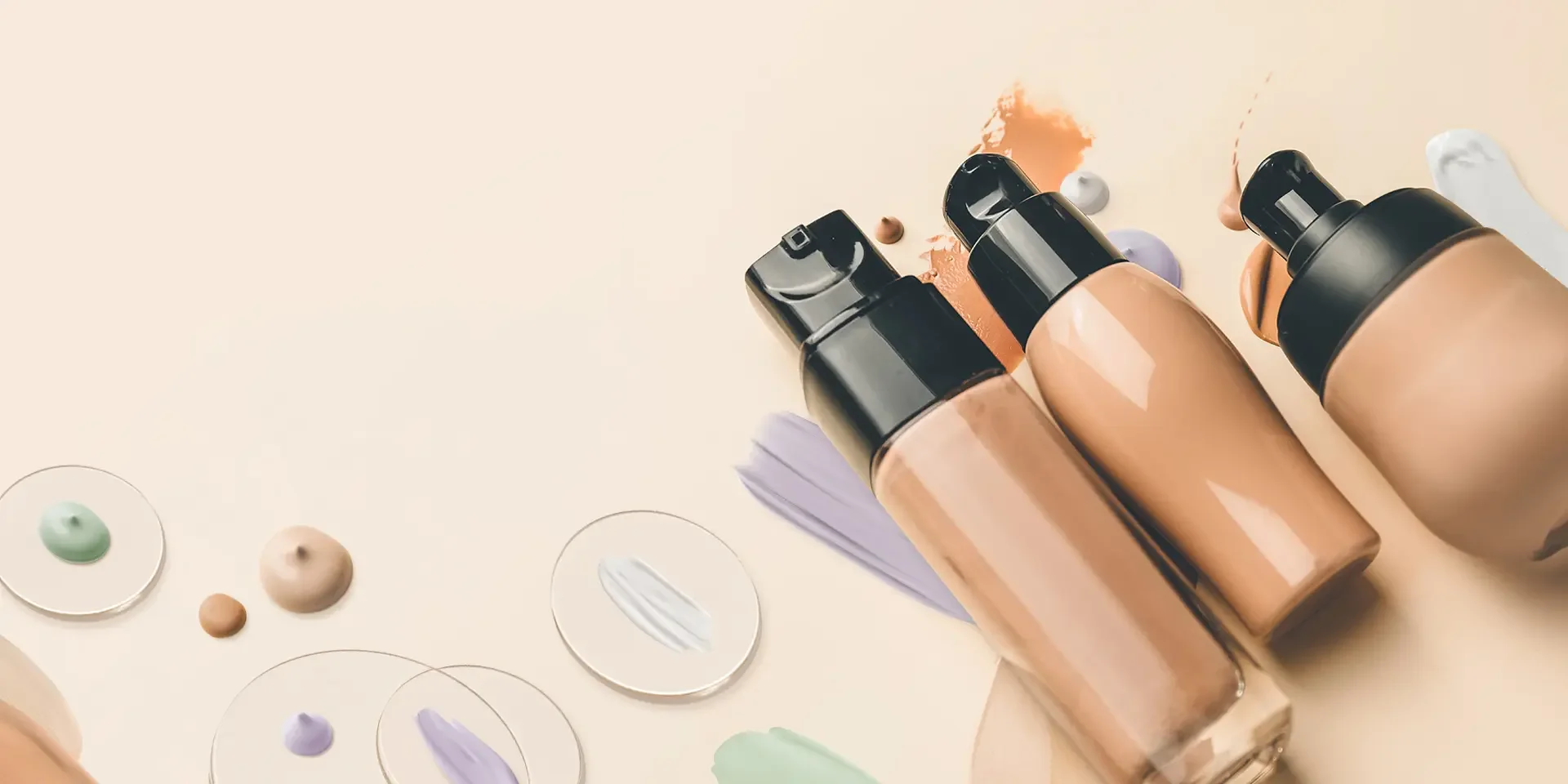 Three foundation bottles with pump caps surrounded by colorful makeup swatches on a light surface.